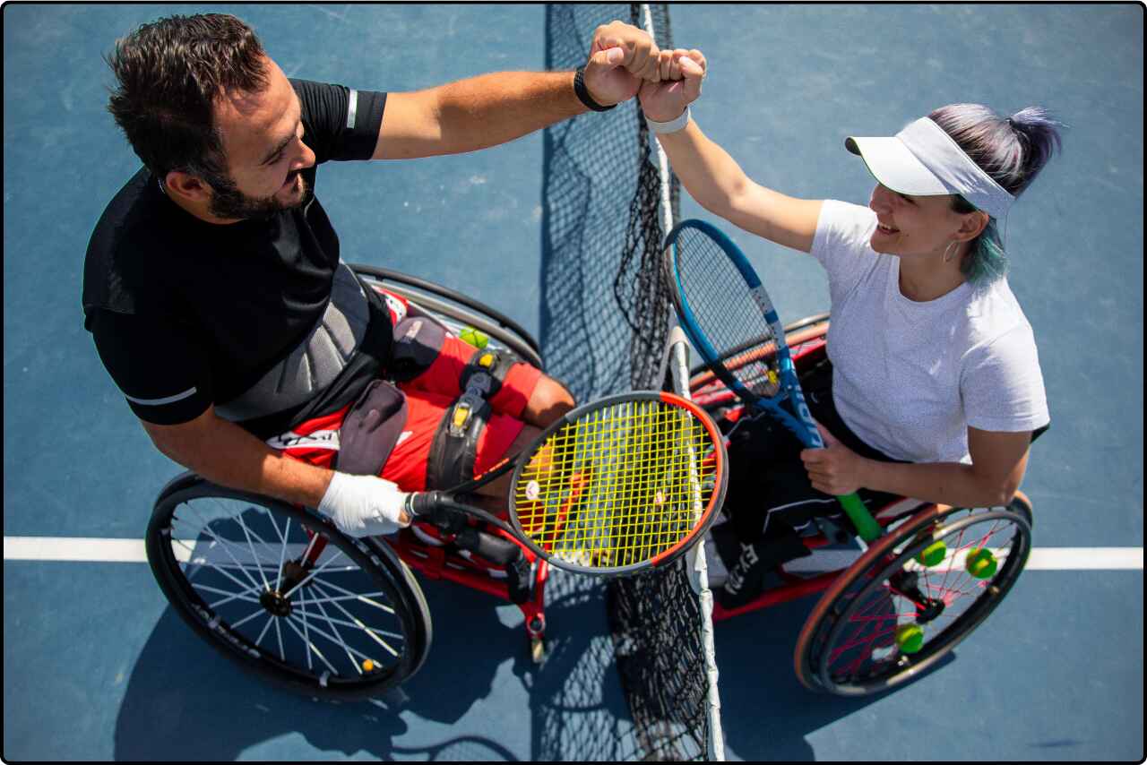 Two athletes with disabilities exchanging a fist bump with smiles after finishing a tennis match.